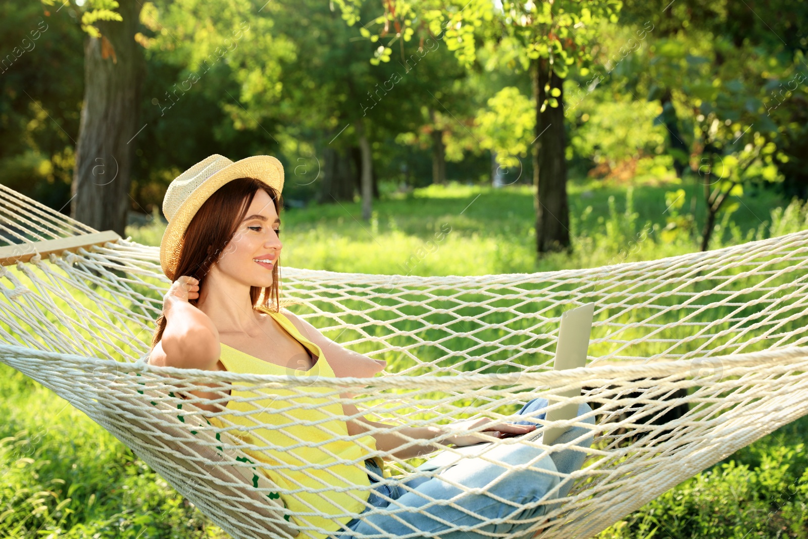 Photo of Young woman with laptop resting in comfortable hammock at green garden