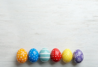 Flat lay composition of painted Easter eggs on wooden table, space for text