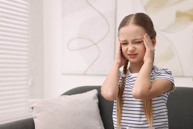 Photo of Little girl suffering from headache on sofa indoors. Space for text