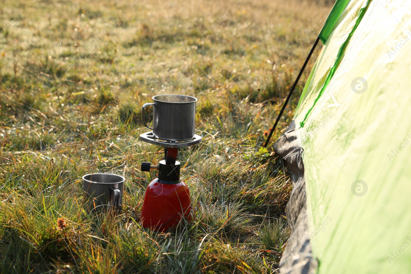 Photo of Portable gas burner with cup near camping tent in mountains