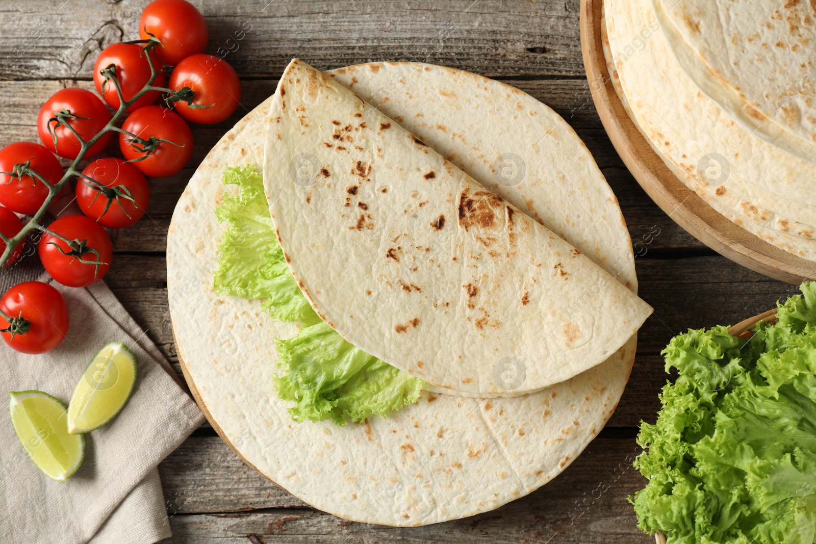 Photo of Tasty homemade tortillas, tomatoes, lime and lettuce on wooden table