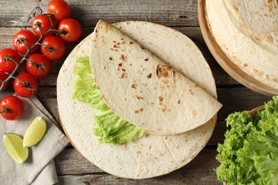 Tasty homemade tortillas, tomatoes, lime and lettuce on wooden table