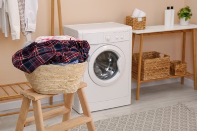 Photo of Wicker laundry basket with clothes on wooden stool in bathroom. Space for text