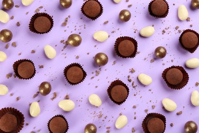 Different delicious chocolate candies on lilac background, flat lay