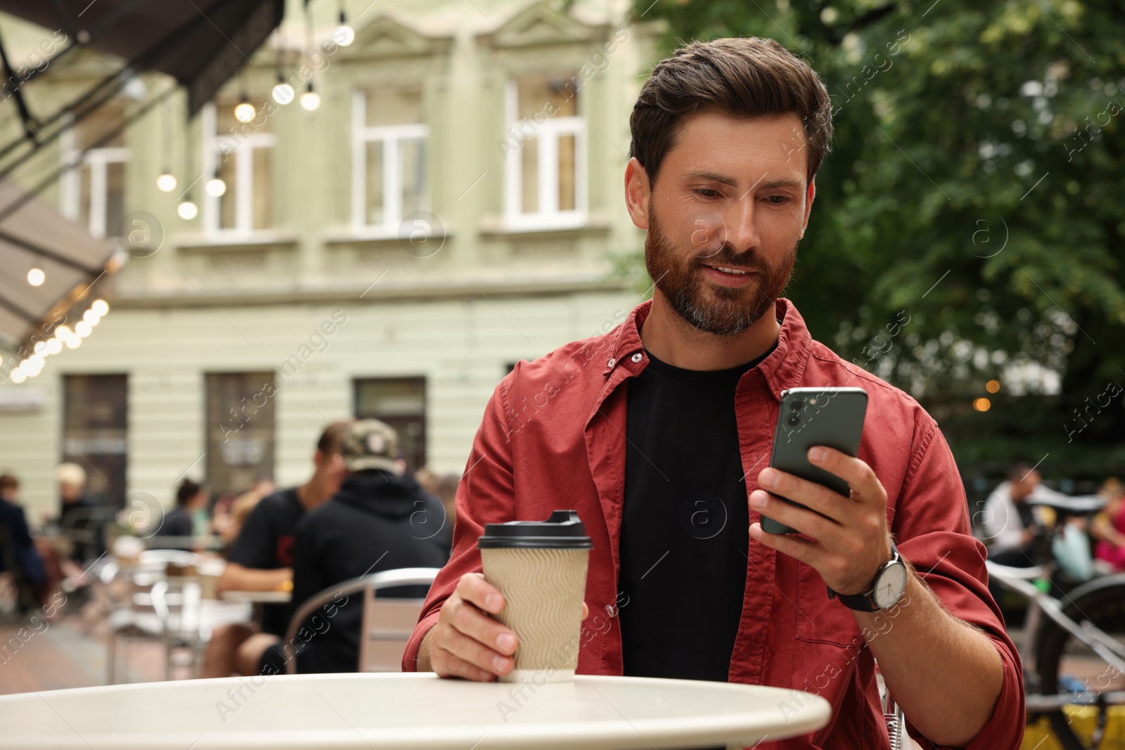 Photo of Handsome man with cup of coffee using smartphone in outdoor cafe, space for text