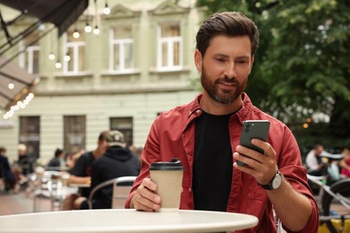 Photo of Handsome man with cup of coffee using smartphone in outdoor cafe, space for text