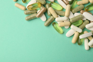 Photo of Different vitamin capsules on turquoise background, top view. Space for text