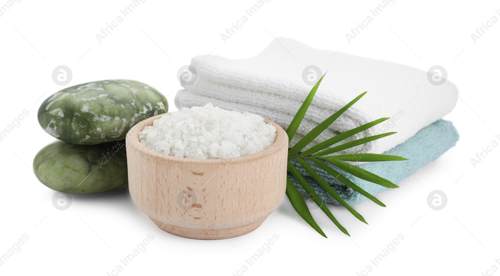 Photo of Bowl of sea salt, towels, massage stones and palm leaf isolated on white. Spa treatment