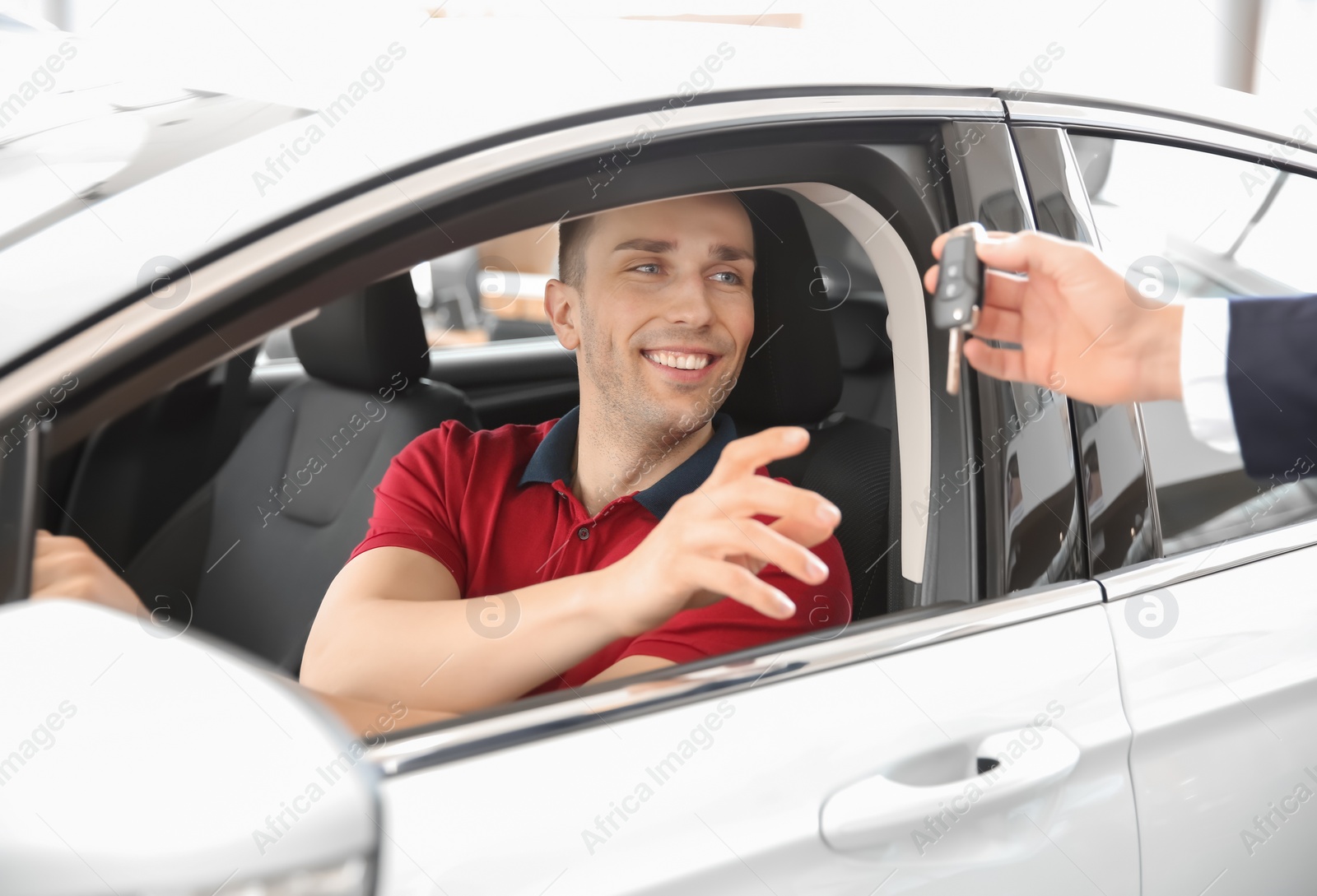 Photo of Salesman passing key to young man in auto at dealership. Buying new car