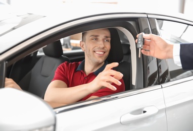 Photo of Salesman passing key to young man in auto at dealership. Buying new car