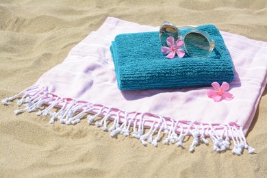 Photo of Blanket with towel, stylish sunglasses and flowers on sand outdoors. Beach accessories