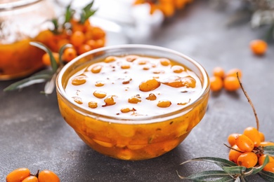 Photo of Delicious sea buckthorn jam and fresh berries on grey table, closeup