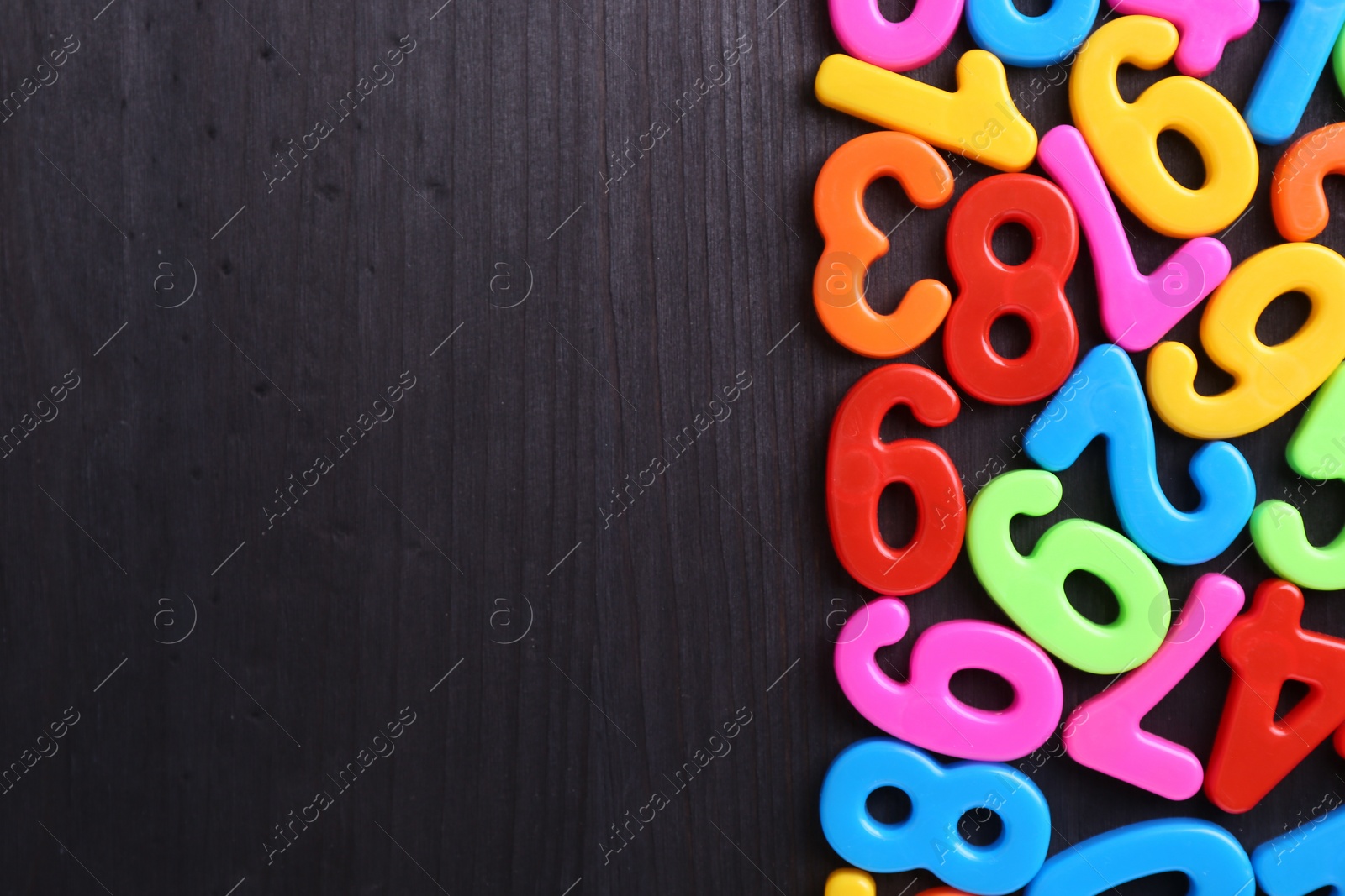 Photo of Colorful numbers on dark wooden school desk, flat lay. Space for text