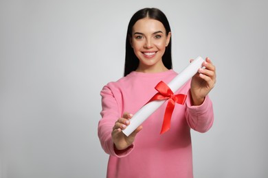 Photo of Happy woman against light grey background, focus on diploma. Space for text