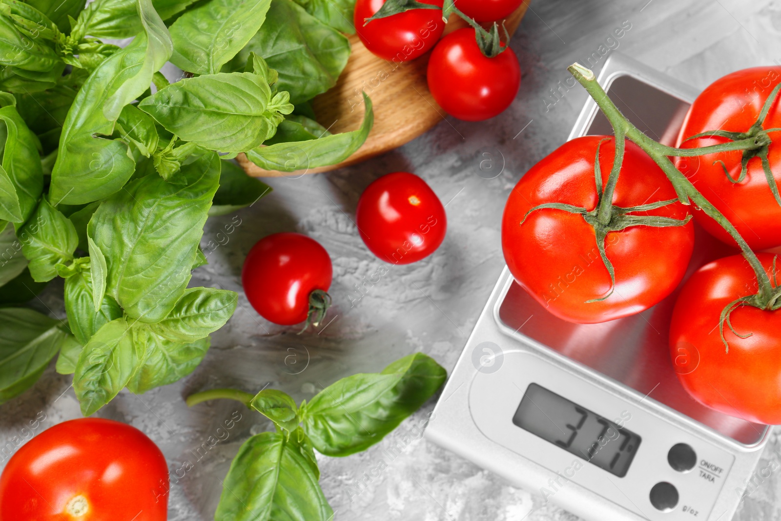 Photo of Kitchen scale with tomatoes and basil on grey textured table, flat lay