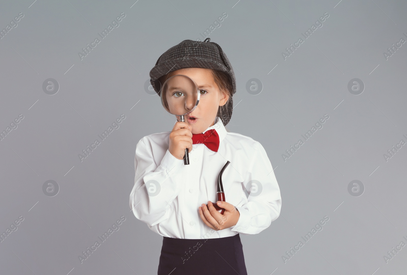 Photo of Cute little child in hat with smoking pipe and magnifying glass playing detective on grey background