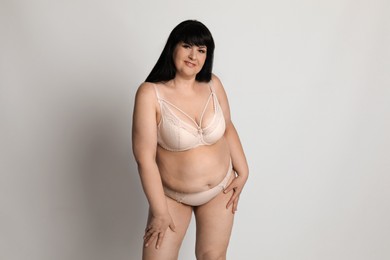 Photo of Beautiful overweight woman in beige underwear on light background. Plus-size model