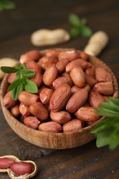 Photo of Fresh unpeeled peanuts and leaves in bowl on wooden table