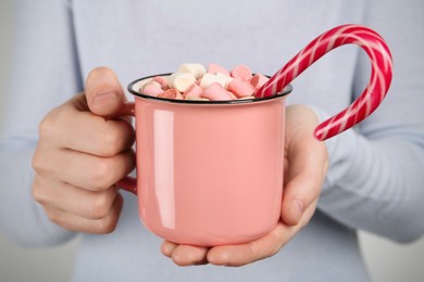 Photo of Woman holding cup of delicious hot chocolate with marshmallows and candy cane, closeup