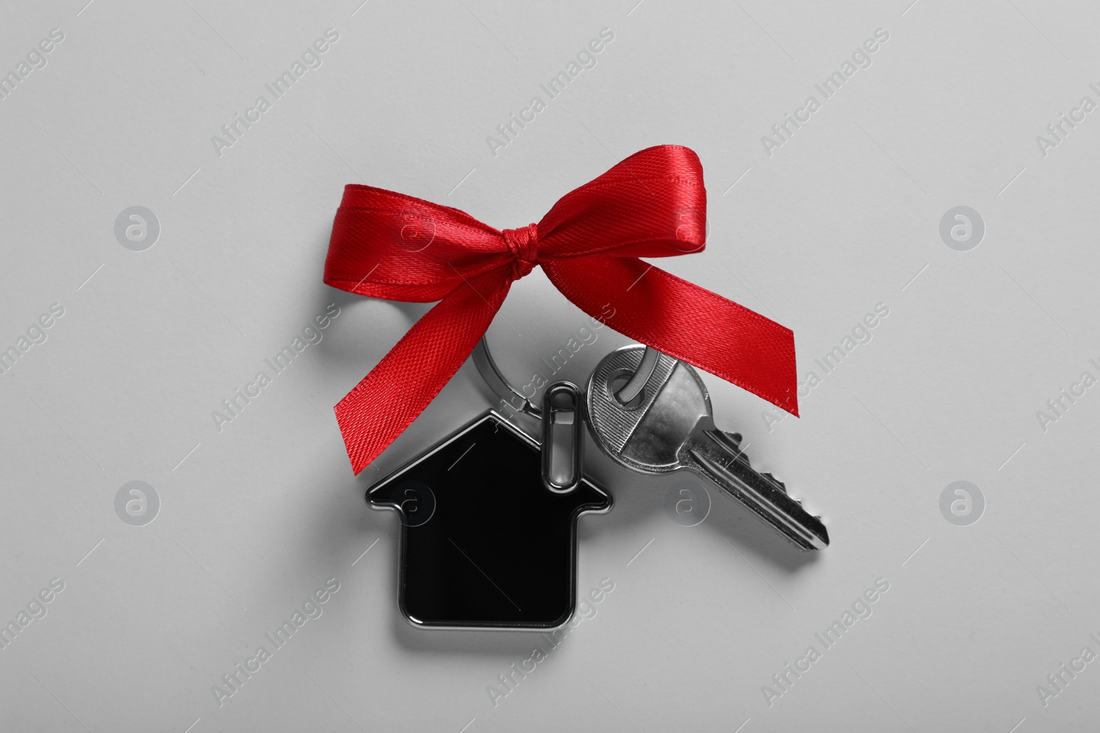 Photo of Key with trinket in shape of house and red bow on light grey background, top view. Housewarming party