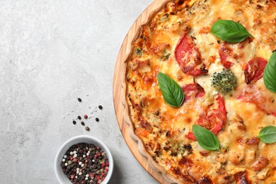 Tasty quiche with cheese, tomatoes and basil leaves on light grey table, flat lay. Space for text