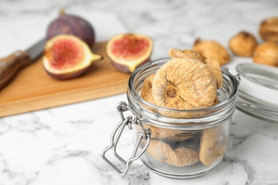 Photo of Glass jar of tasty dried figs on marble table. Space for text