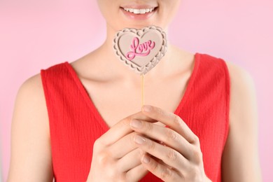 Photo of Woman holding heart shaped lollipop made of chocolate on pink background, closeup