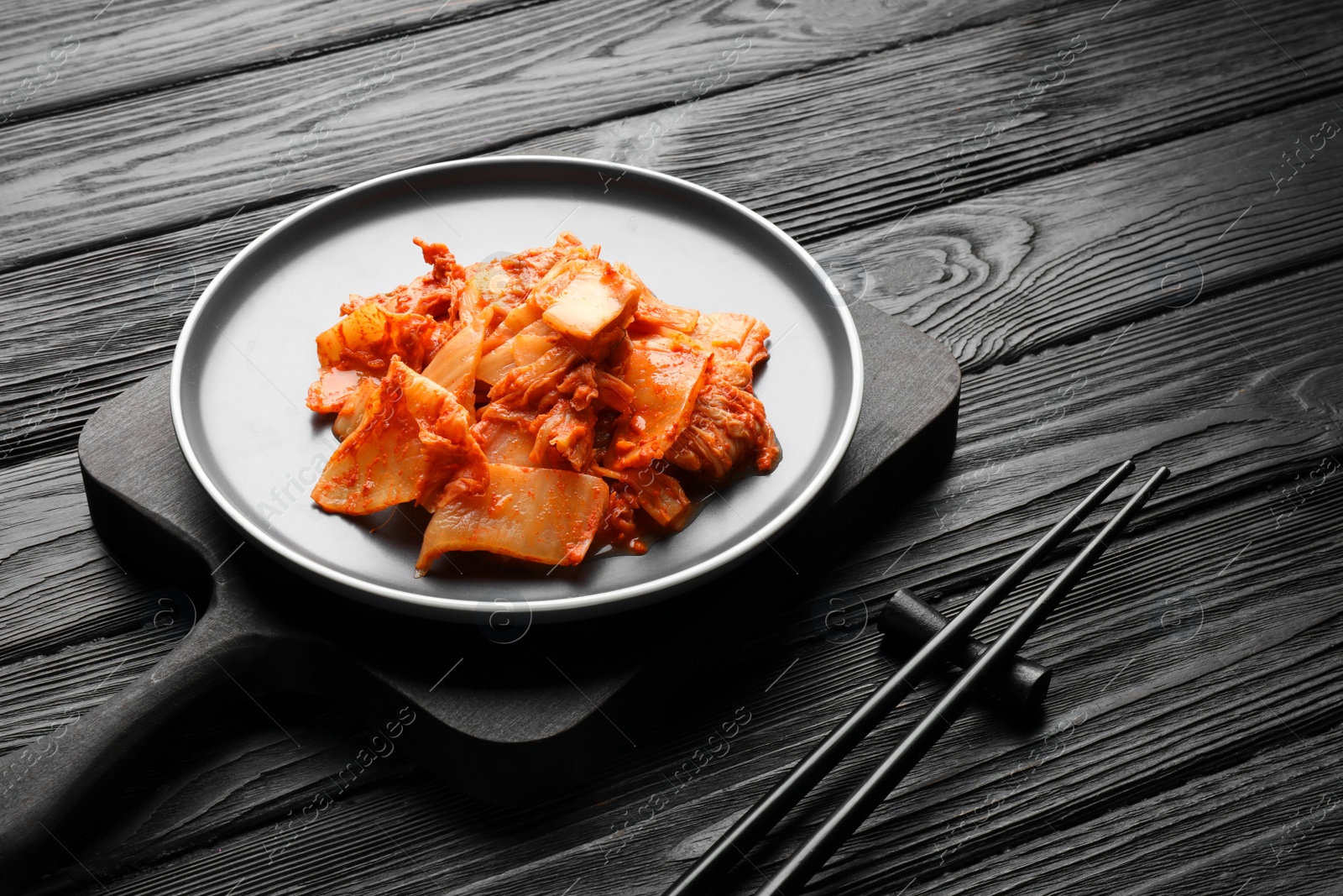 Photo of Delicious kimchi with Chinese cabbage served on black wooden table