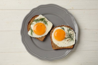 Plate with tasty fried eggs, slices of bread and dill on white wooden table, top view