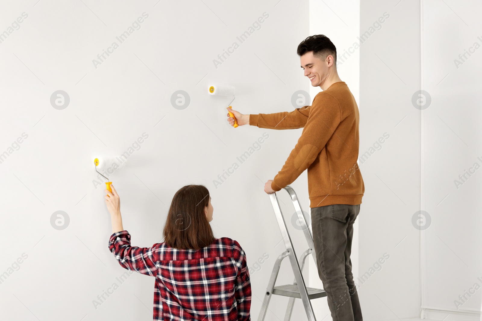 Photo of Young couple painting wall with rollers indoors. Room renovation