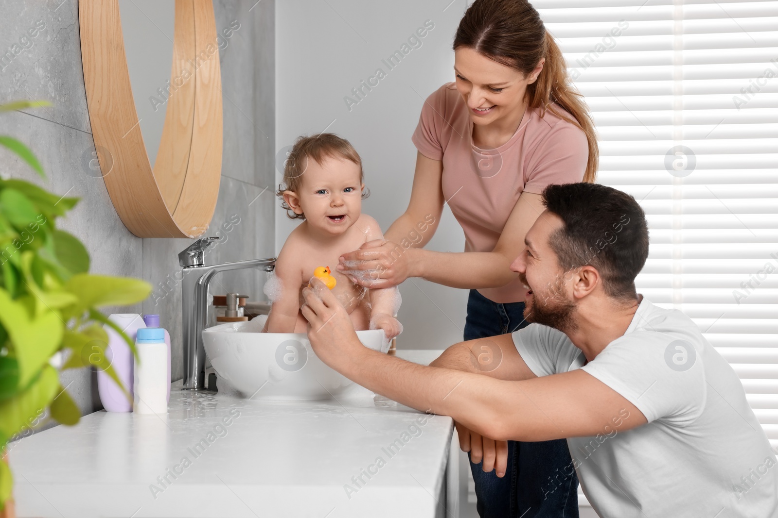 Photo of Father and mother washing their little baby in sink at home