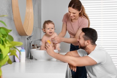 Father and mother washing their little baby in sink at home