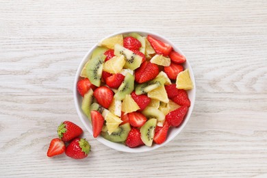 Photo of Delicious fresh fruit salad in bowl on white wooden table, top view