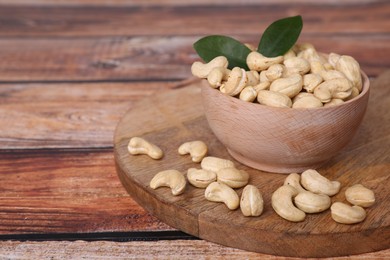 Photo of Tasty cashew nuts and green leaves on wooden table, space for text