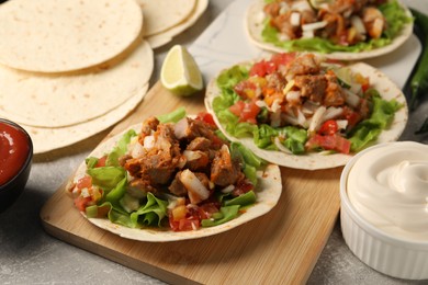Photo of Delicious tacos with vegetables, meat and sauce on grey textured table
