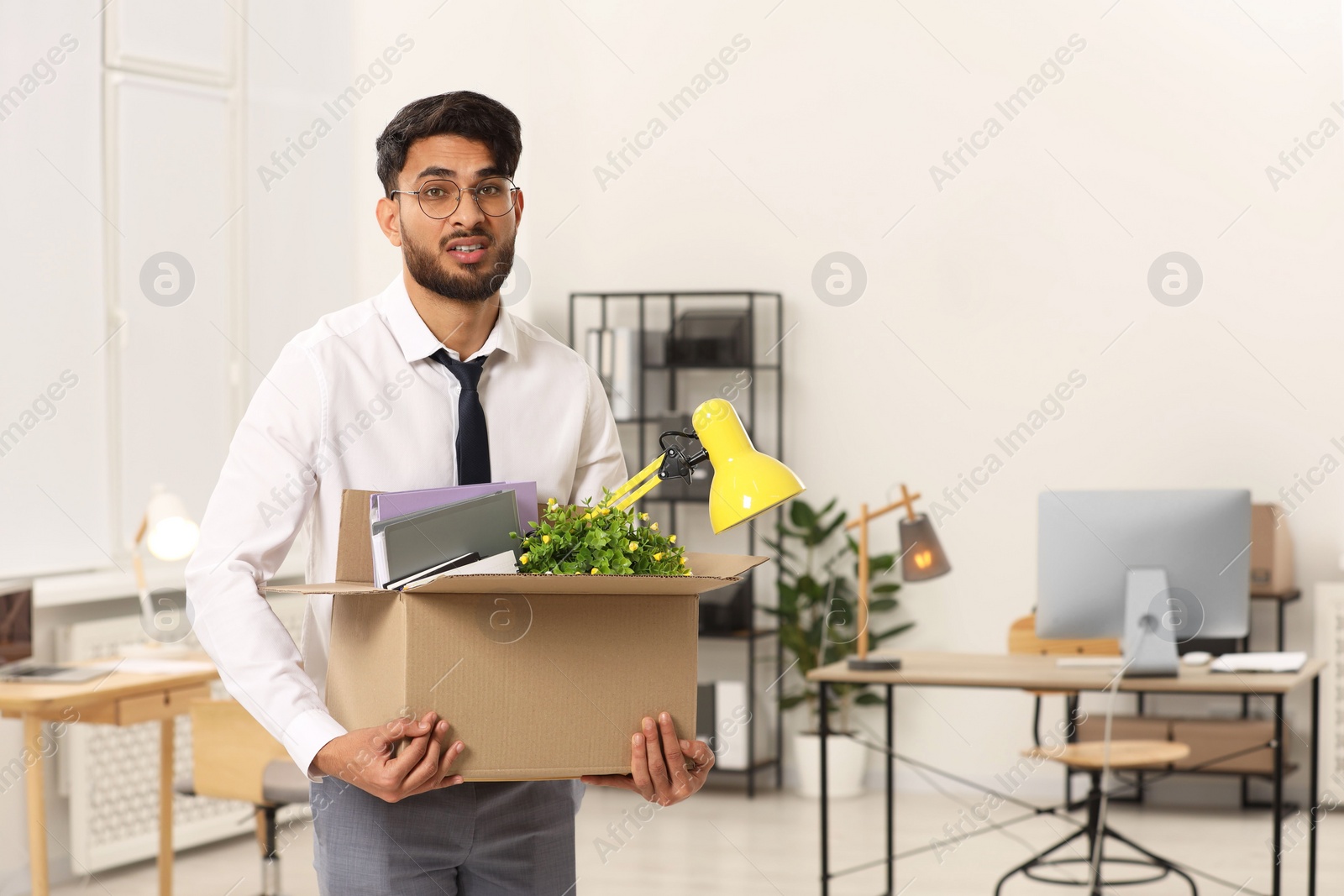 Photo of Unemployment problem. Frustrated man with box of personal belongings in office