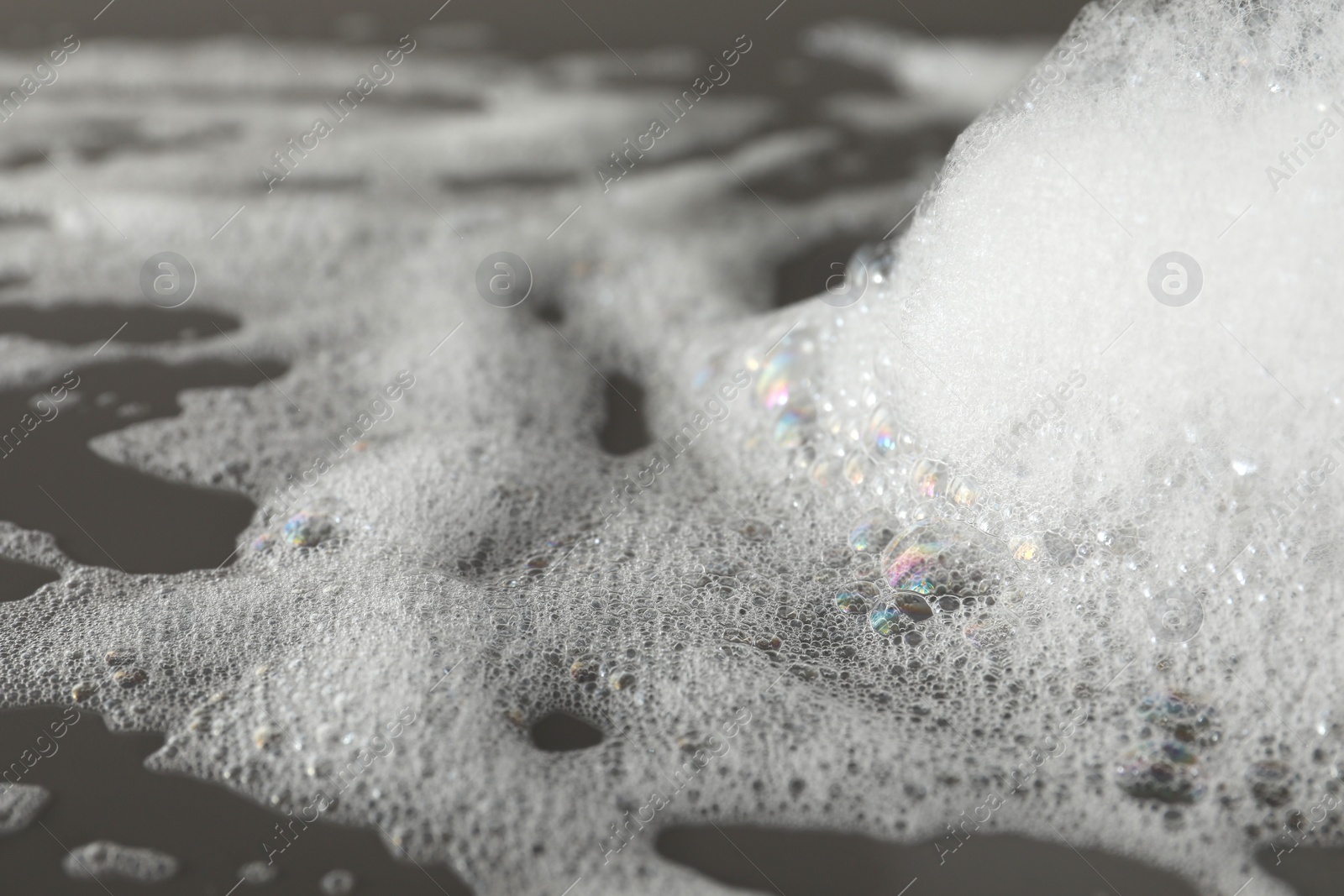 Photo of Fluffy bath foam on grey background, closeup