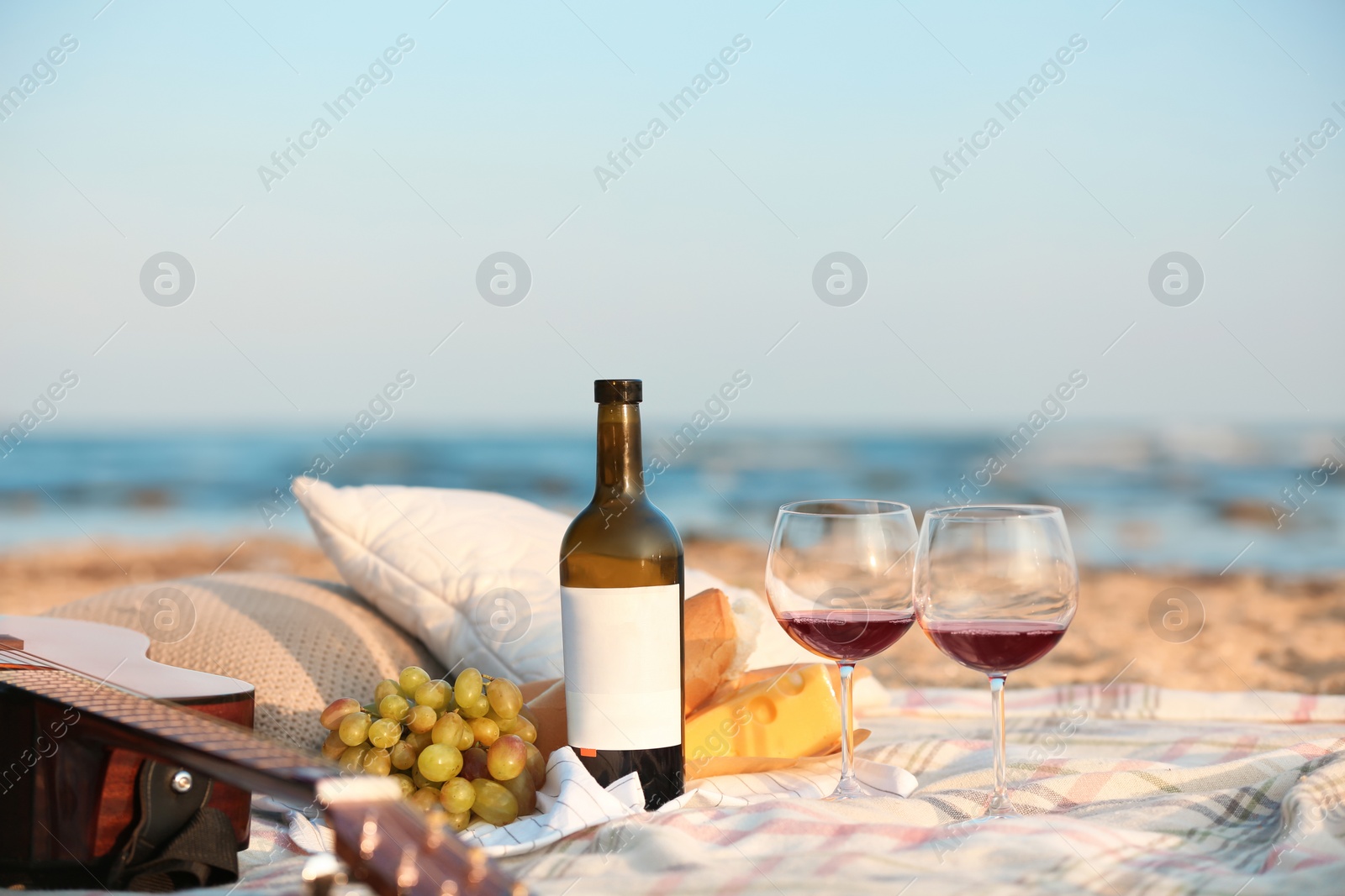 Photo of Blanket with food, wine and guitar on beach. Romantic picnic for couple