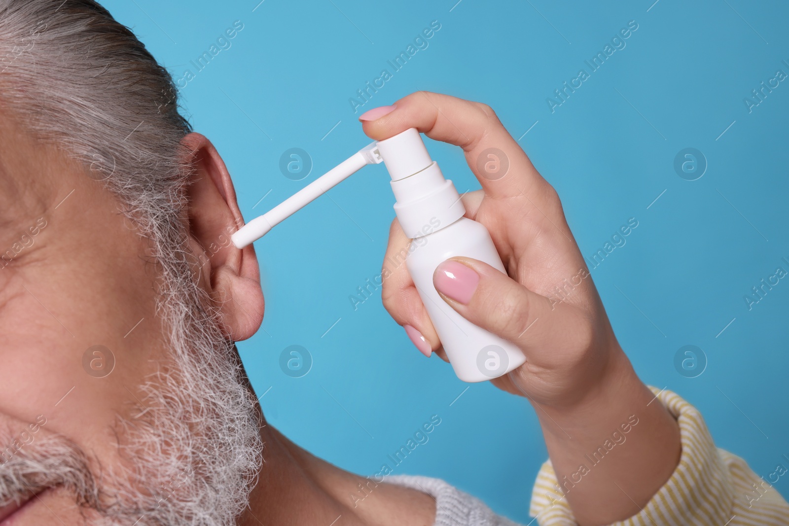 Photo of Young woman spraying medication into man's ear on light blue background, closeup