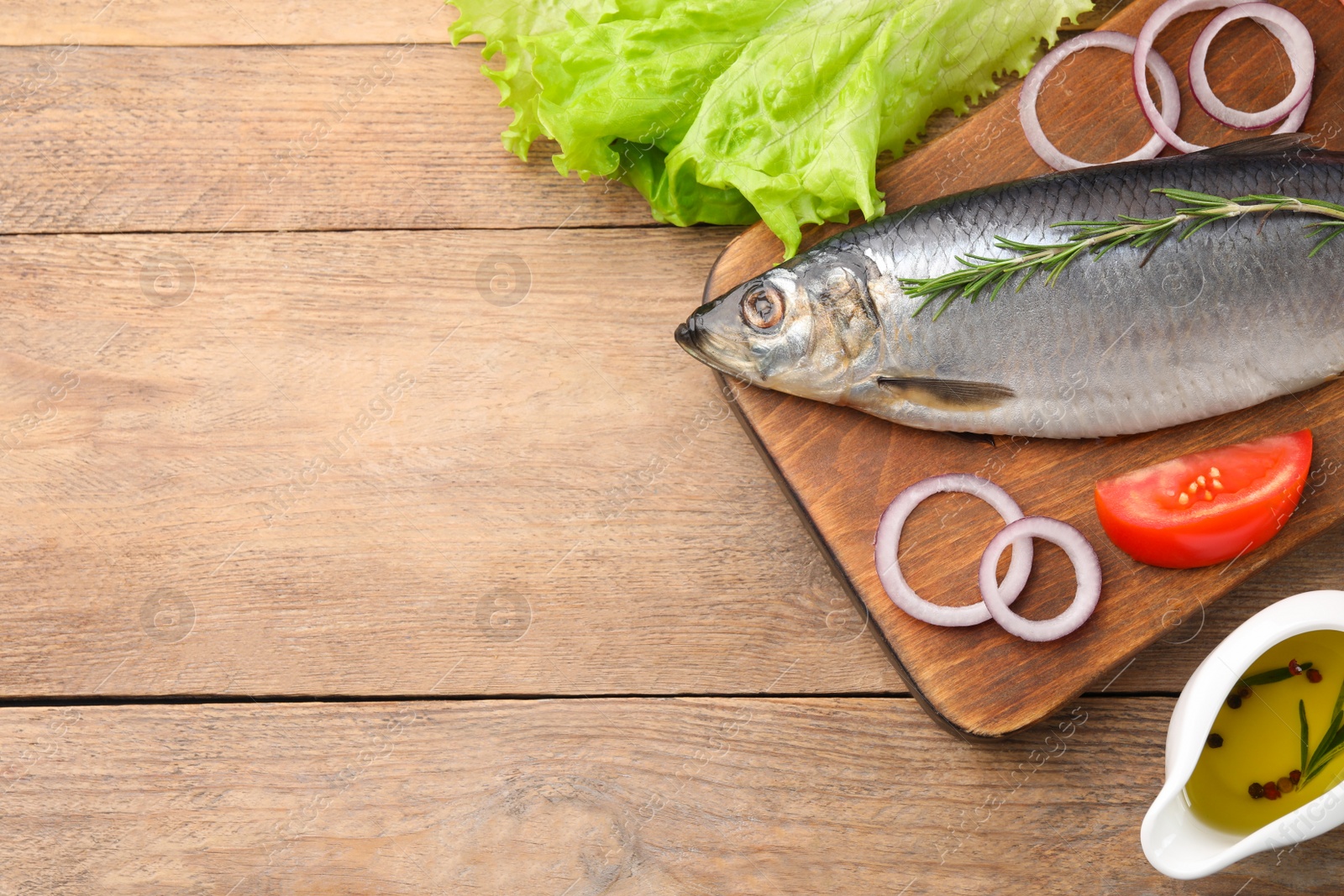 Photo of Board with delicious salted herring and ingredients on wooden table, flat lay. Space for text