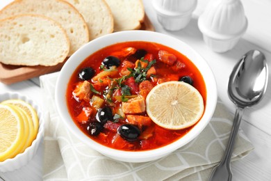 Photo of Meat solyanka soup with sausages, olives and vegetables served on white wooden table