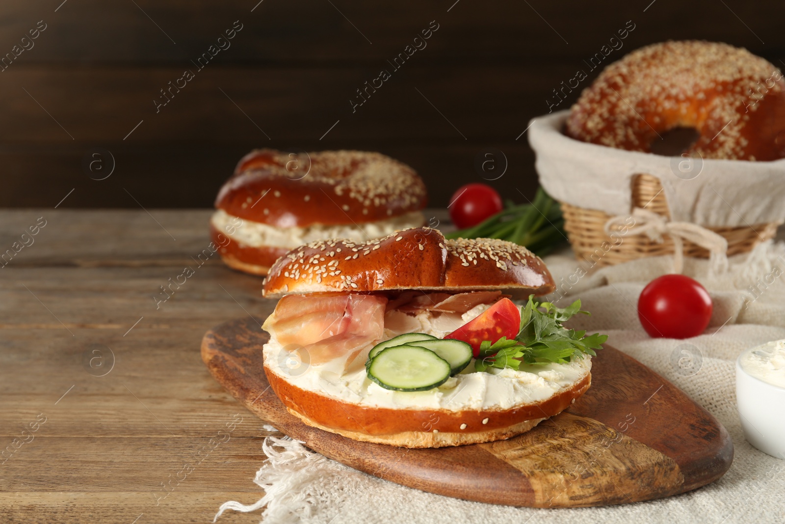 Photo of Delicious bagel with cream cheese, jamon, cucumber, tomato and parsley on wooden table