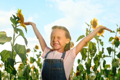 Photo of Cute little girl with sunflowers outdoors. Child spending time in nature