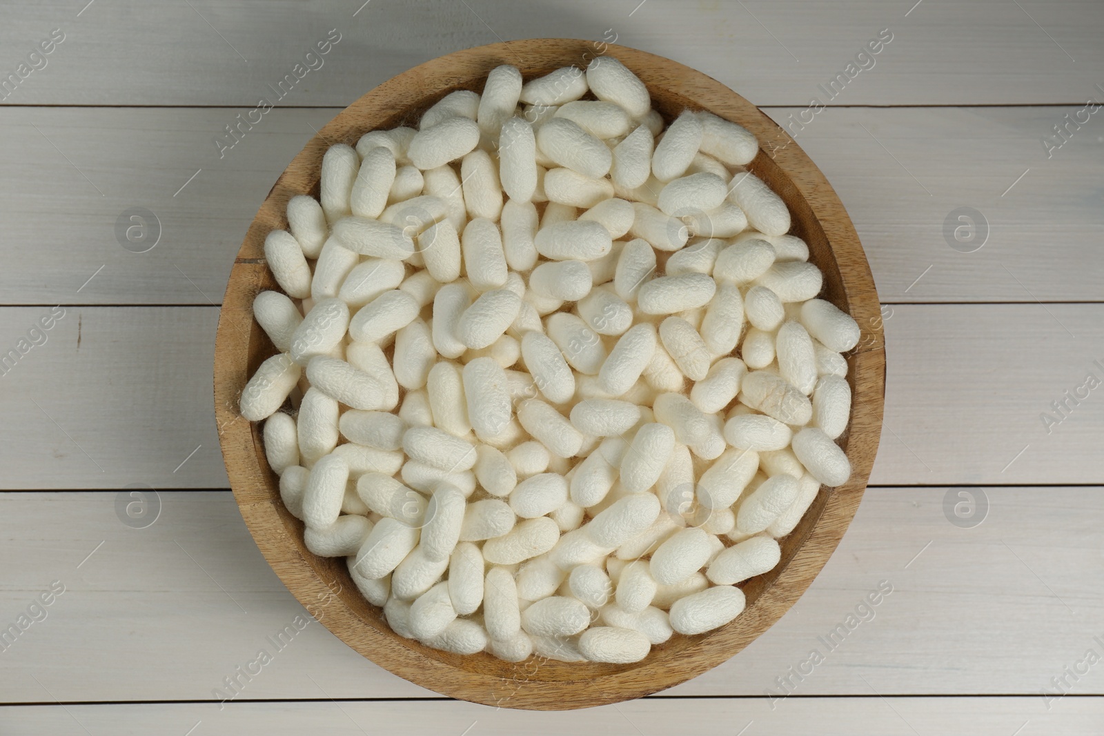 Photo of Silk cocoons in bowl on white wooden table, top view