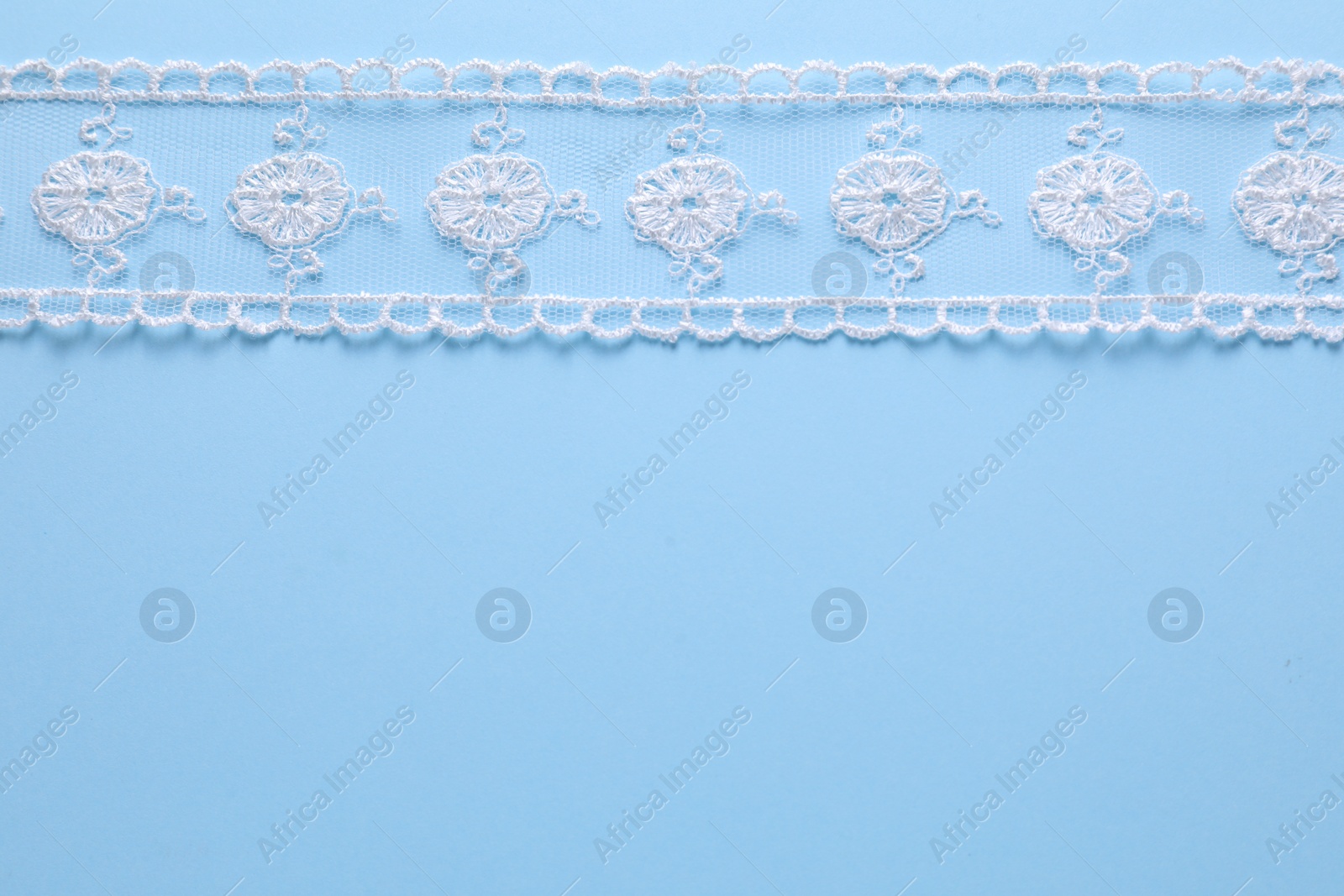 Photo of White lace on light blue background, top view. Space for text