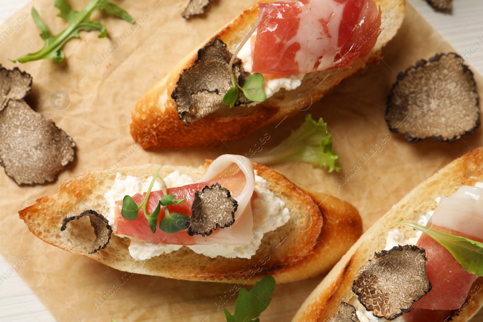 Photo of Delicious bruschettas with cheese, prosciutto and slices of black truffle on white table, closeup