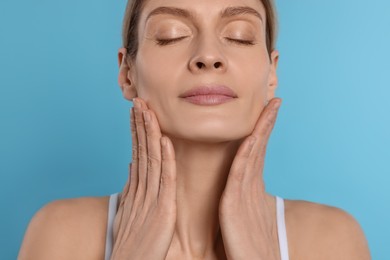 Photo of Woman massaging her face on turquoise background