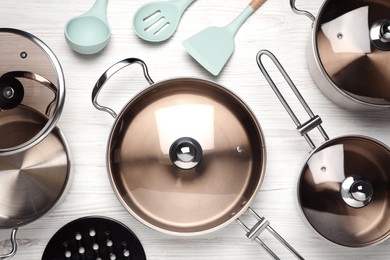 New cookware set and kitchen utensils on white wooden table, flat lay