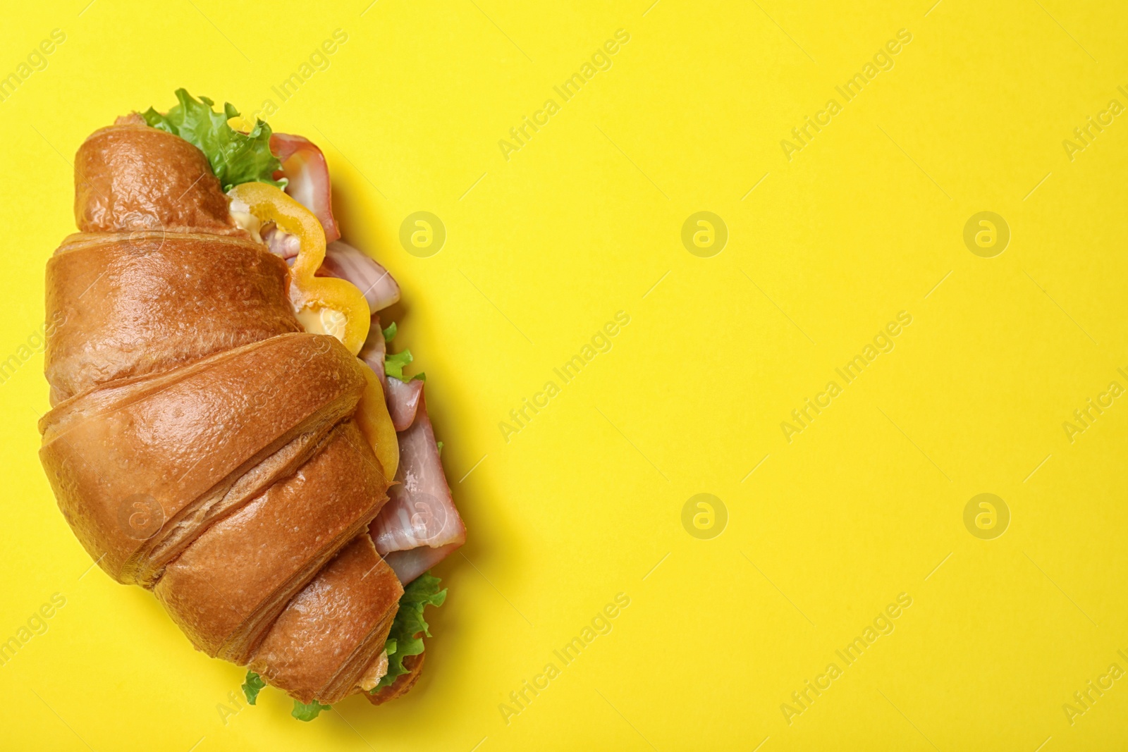 Photo of Tasty croissant sandwich with ham on yellow background, top view. Space for text