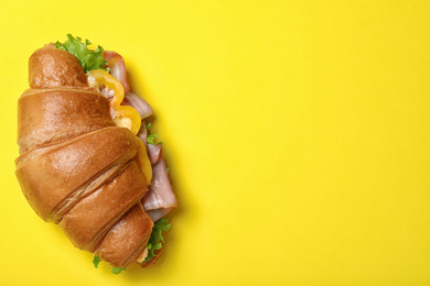 Tasty croissant sandwich with ham on yellow background, top view. Space for text